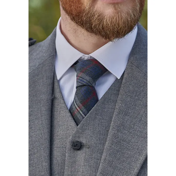 Close up on a tartan tie worn by a man in a standard collar white shirt, jacket and waistcoat.